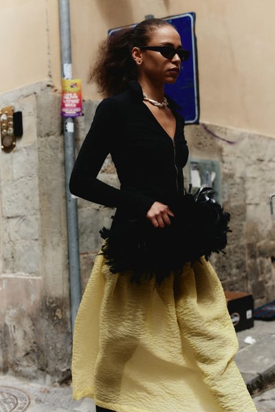 woman in a black shirt with a yellow skirt and a feather bag.